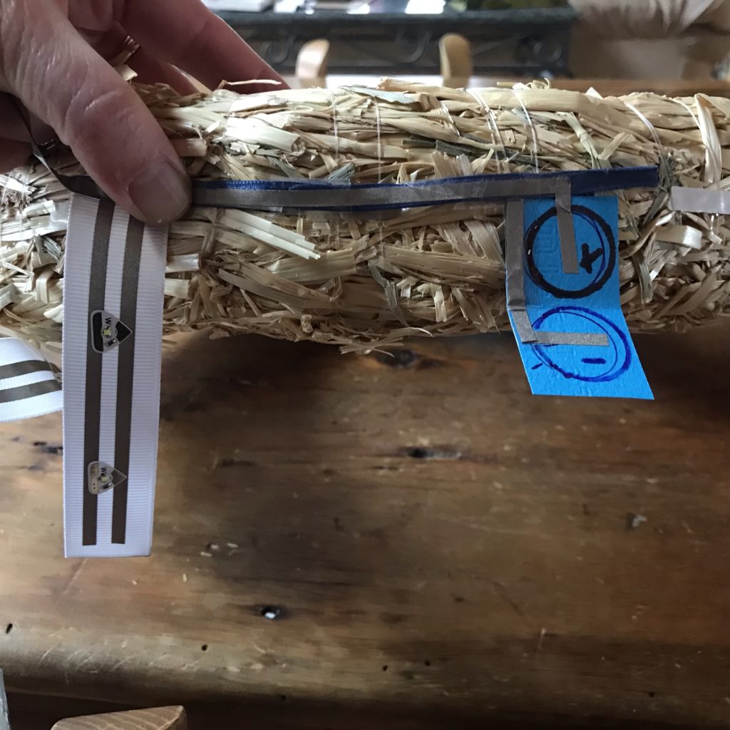 A blue paper battery holder hangs down from a ribbon rail that has conductive fabric tape on both sides of it.
