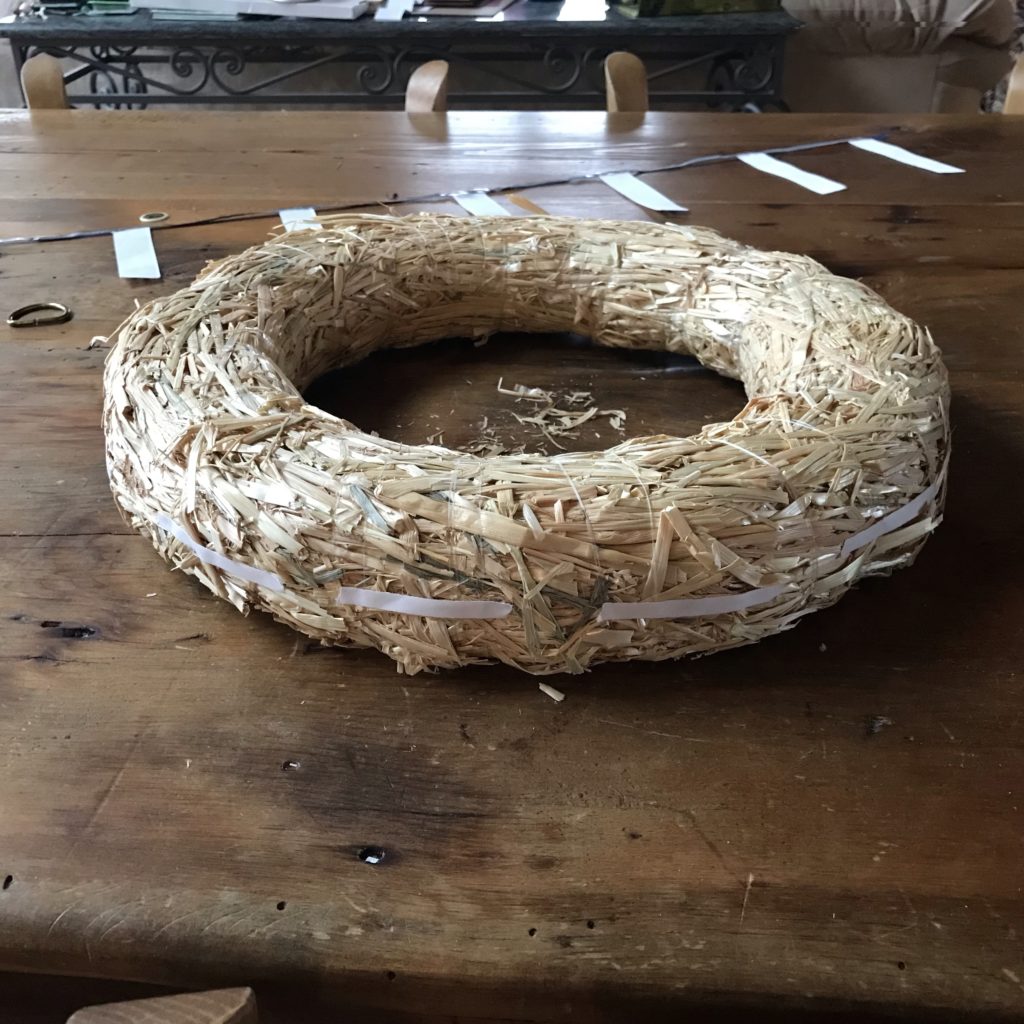 A straw wreath with double-sided tape around its circumference sits upon a wooden table.