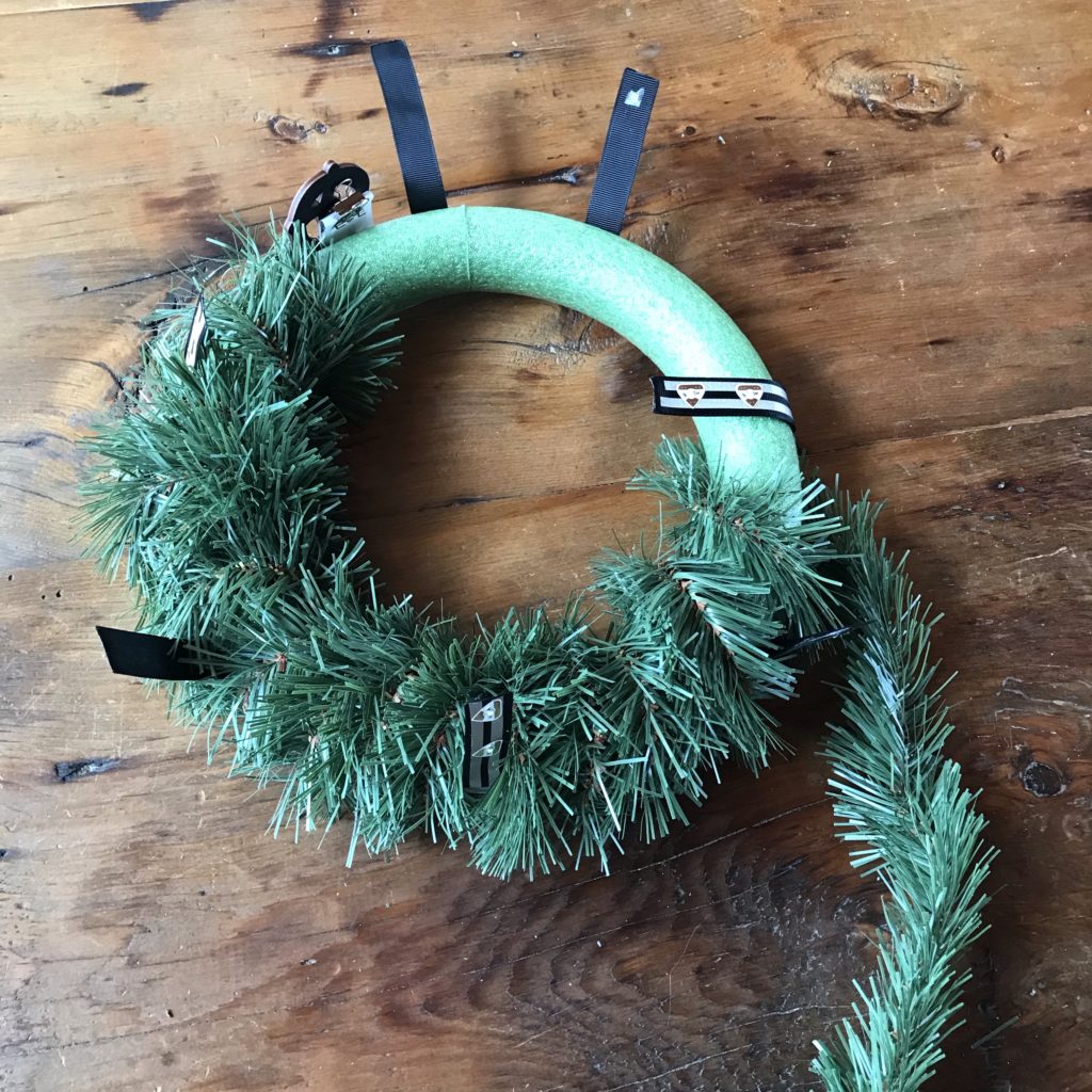 A strand of pine tinsel if wrapped around the green foam wreath form to disguise the location of the ribbon rail.