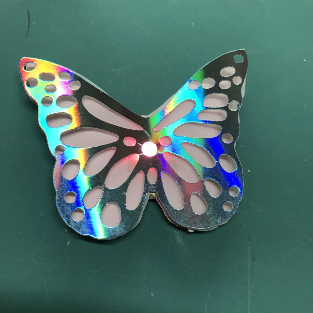 A decorative piece of butterfly-shaped paper with a variety of lacy cut-outs has been adhered on top of glowing butterfly with a translucent vellum layer underneath.