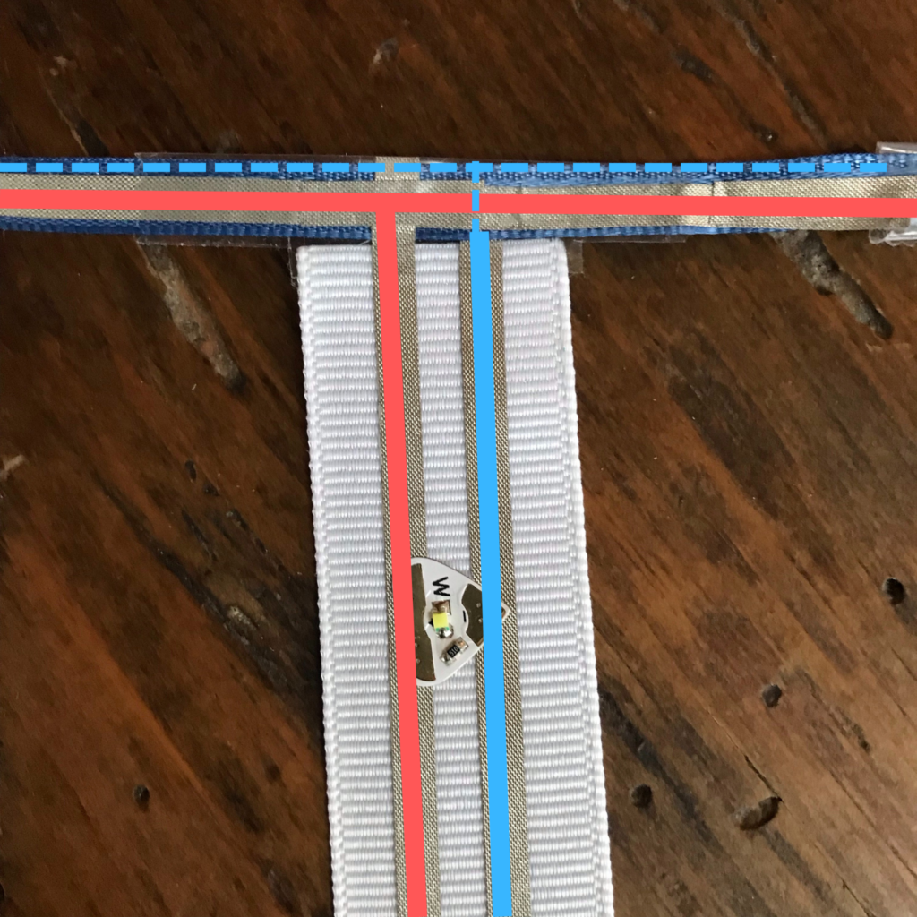 Close-up, color coded LED branch attached to the ribbon rail. The positive lead on the front side of the ribbon is red.  The negative lead on the back side of the ribbon is blue. S single LED sticker bridges the gap.  The positive and negative traces do not touch one another.