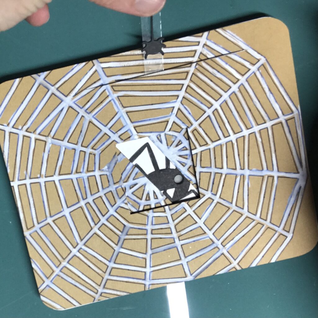 A cut-out of a paper spider has been adhered on top of a clear acetate lever to conceal a magnet.