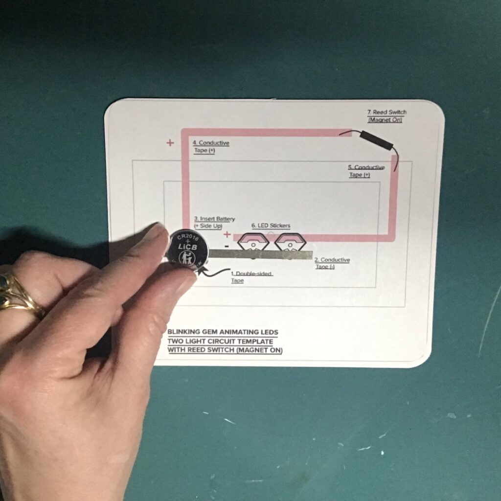 A CR2016 coin cell battery is being placed upon the circular footprint on a circuit diagram.