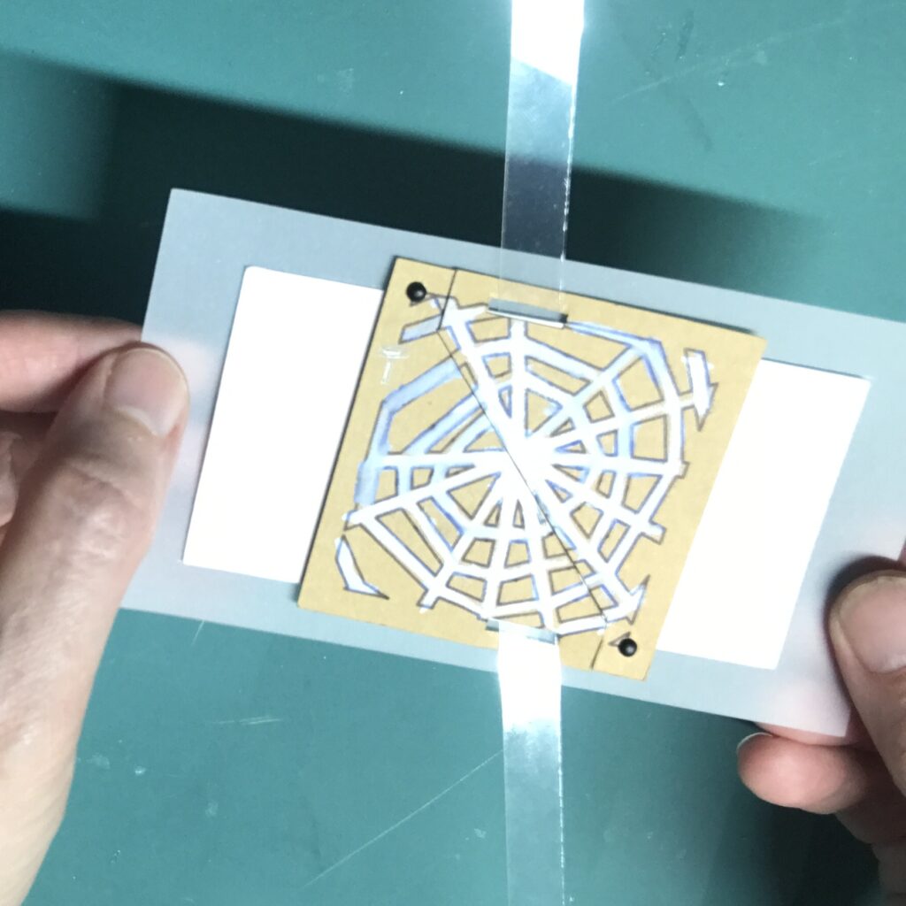 Two pieces of a tabbed paper door (cut diagonally) have been placed onto the top and bottom ends of a clear strip of acetate, anchored to the center of a white piece of vellum. The diagonal doors have been secured with metal brads.