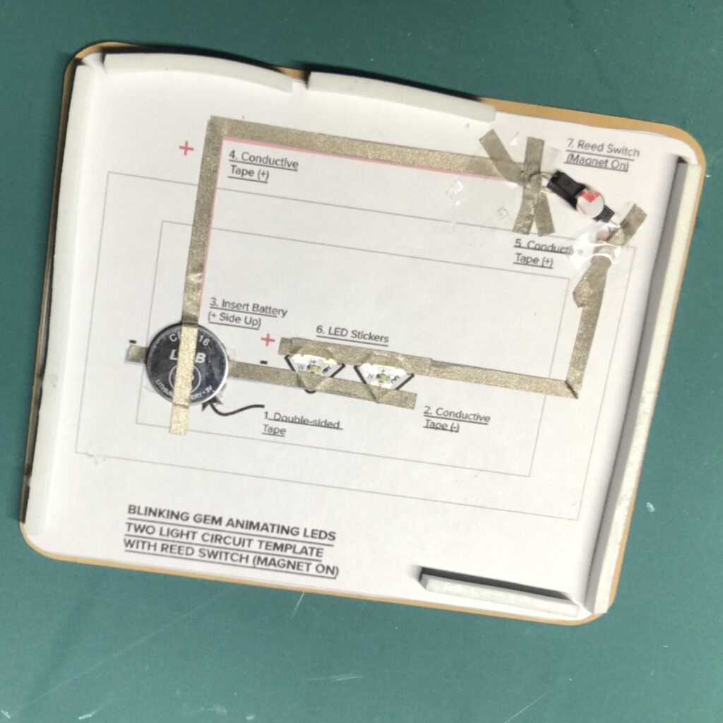 A rectangular card back with a Circuit Diagram attached to it has foam tape strips along most of its perimeter.