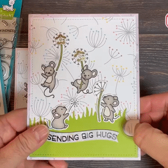 Two hands hold a rectangular card with a pull-tab in the bottom right-hand corner. The bottom of the card reads "Sending Big Hug," centered below a group of five cartoonish mice. Two mice are holding onto dandelion flowers that have flower-shaped Animating LEDs in their centers. These Rainbow Fade Animating LED stickers are cycling through the colors of the rainbow.