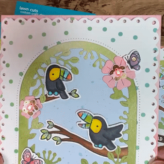 A close-up view of a handmade card depicting a pair of toucans sitting upon two different branches of a tree. Flower-shaped animating LEDs change colors in the tree canopy.