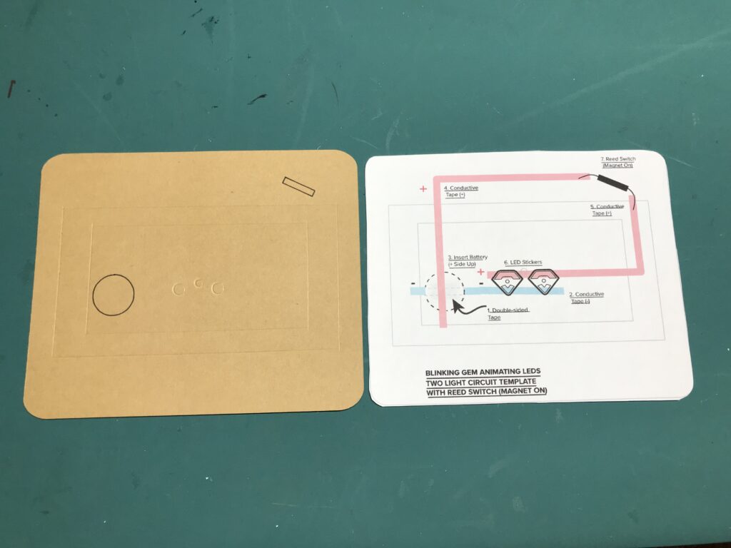 The card back made with a Cricut smart cutting machine is placed next to a printed circuit diagram of the same size and dimensions.