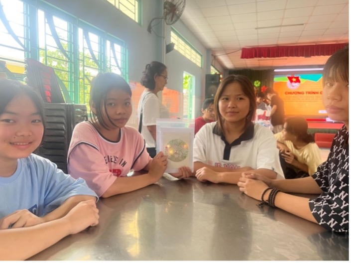 Four girls sit at a table, proudly holding a white light-up card with three spots of light in the center.