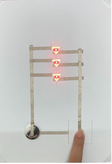 A finger presses on a switch and three LED Stickers, stacked in a vertical line, glow red.