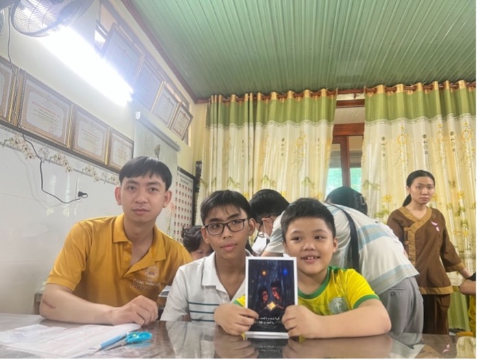 Three boys sit at a table, proudly holding a black light-up card with a spot of light in the center.