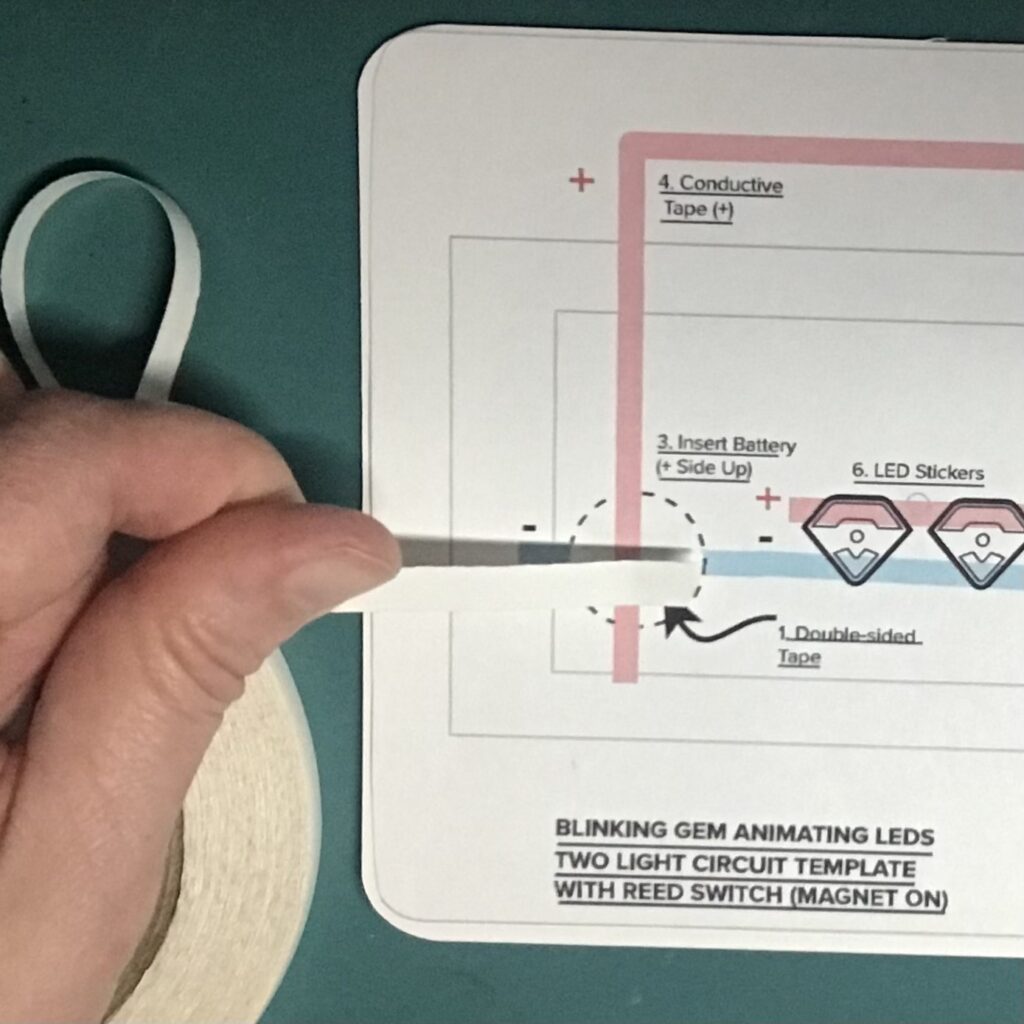 A piece of double-sided tape is being placed in the round footprint denoting where a coin cell battery will be placed.