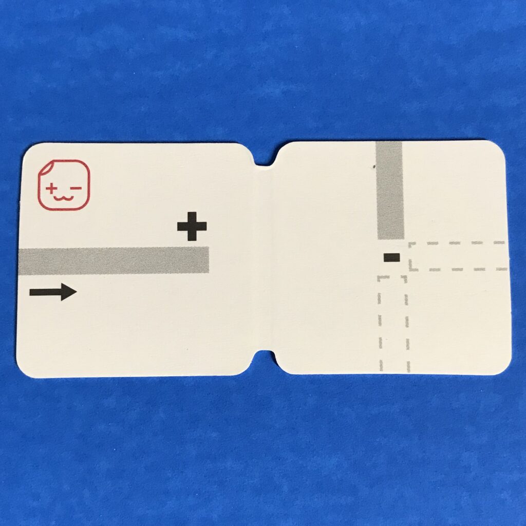 A white, rectangular piece of cardstock that is a folding paper battery holder, rests against a blue background.  The left side depicts where the positive trace of a circuit should be applied.  The right side shows markings representing different locations for where the negative lead of the circuit may be applied.